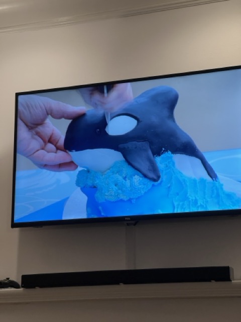 A photo of the Netflix show Great British Bakeoff, focused on Paul Hollywood cutting open an Orca Cake